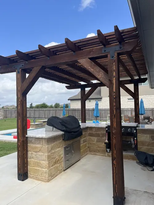 Cedar pergola and stone outdoor kitchen with a granite counter and built-in grill cabinet